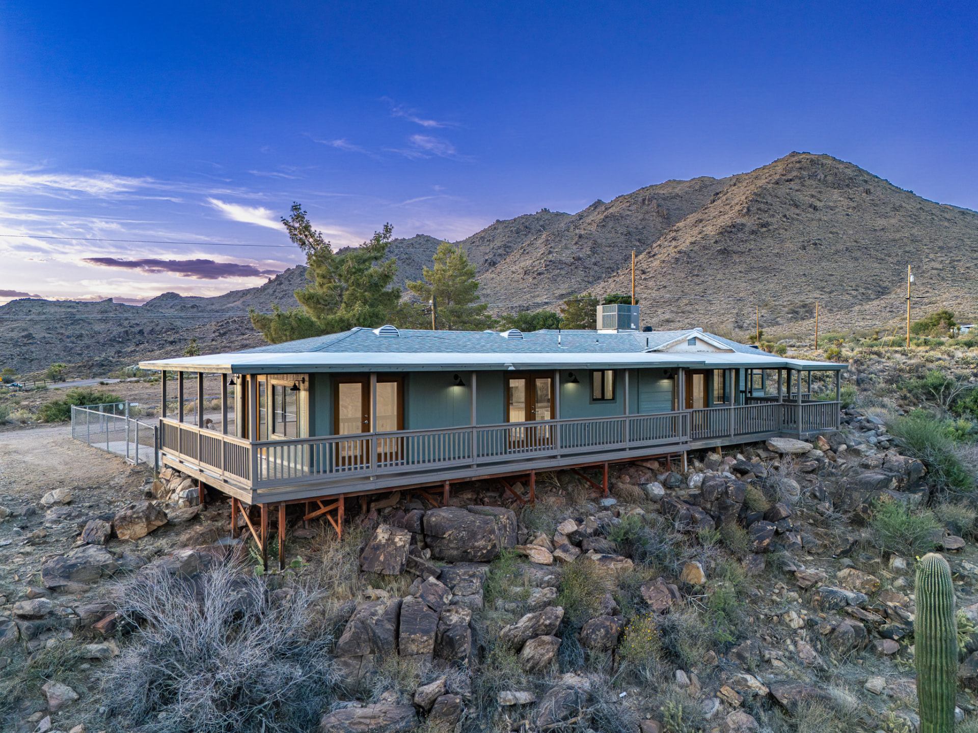 Cinematic twilight drone photo of a desert home with glowing interior lights and mountain backdrop